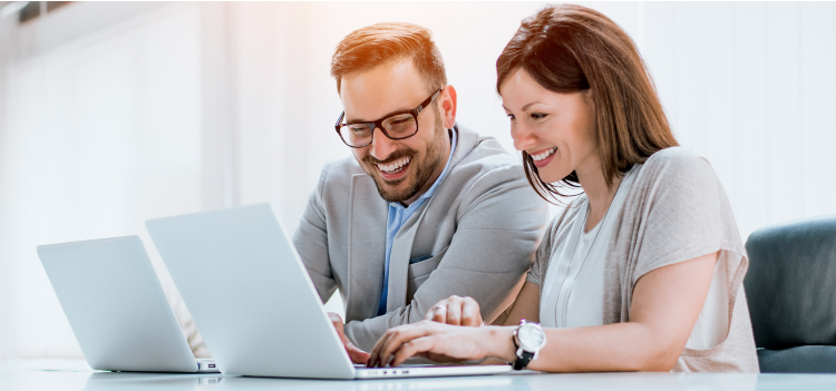 Photo of a man and woman smiling looking at their computers 